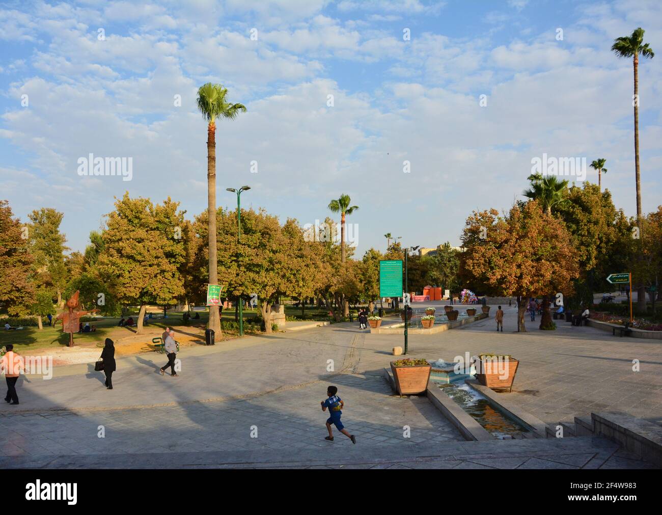 Shiraz, Iran : entrée au parc Azadi depuis le boulevard Azadi. Vue vers le sud-est. Les gens qui marchent dans le parc. Un enfant qui s'exécute dans le f Banque D'Images