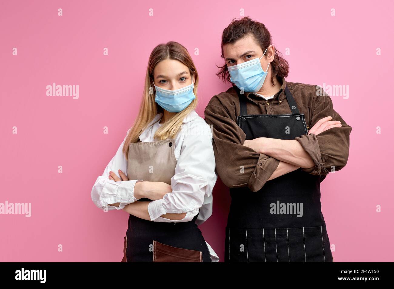 Les serveurs sérieux et confiants se tiennent avec les bras repliés, prêts à servir les clients pendant COVID-19, portrait de l'homme et de la femme dans l'isolat de masque de protection médicale Banque D'Images