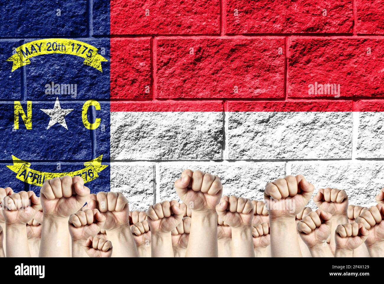 Des poings élevés sur le fond de l'État du pavillon représenté de Caroline du Nord sur un mur de briques, un concept de force et d'unité. Banque D'Images