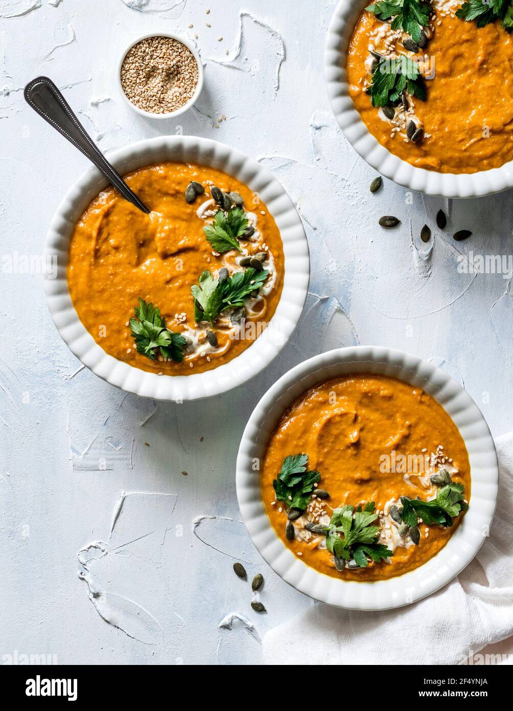 Trois bols de soupe de potiron chaude, réconfortante, très crémeuse, vegan au curry, garnie de yaourt végétalien, d'herbes fraîches, de citrouille et de graines de sésame. Banque D'Images