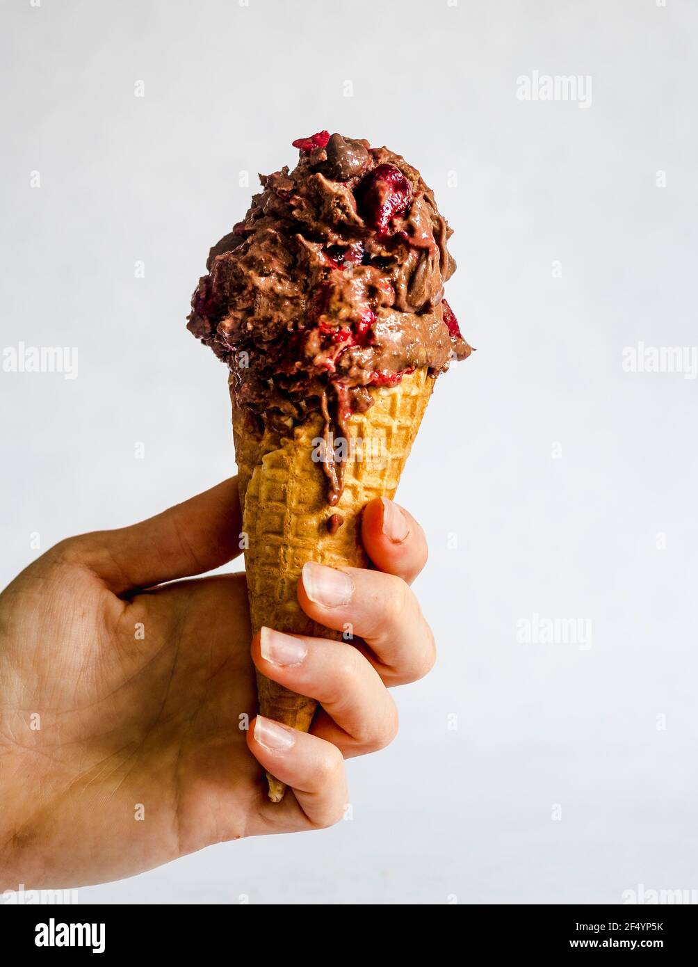 Main tenant la fonte, maison, sans-chourn vegan doux chocolat glace avec des chips de chocolat et des cerises hachées. Un plaisir d'été parfait. Banque D'Images