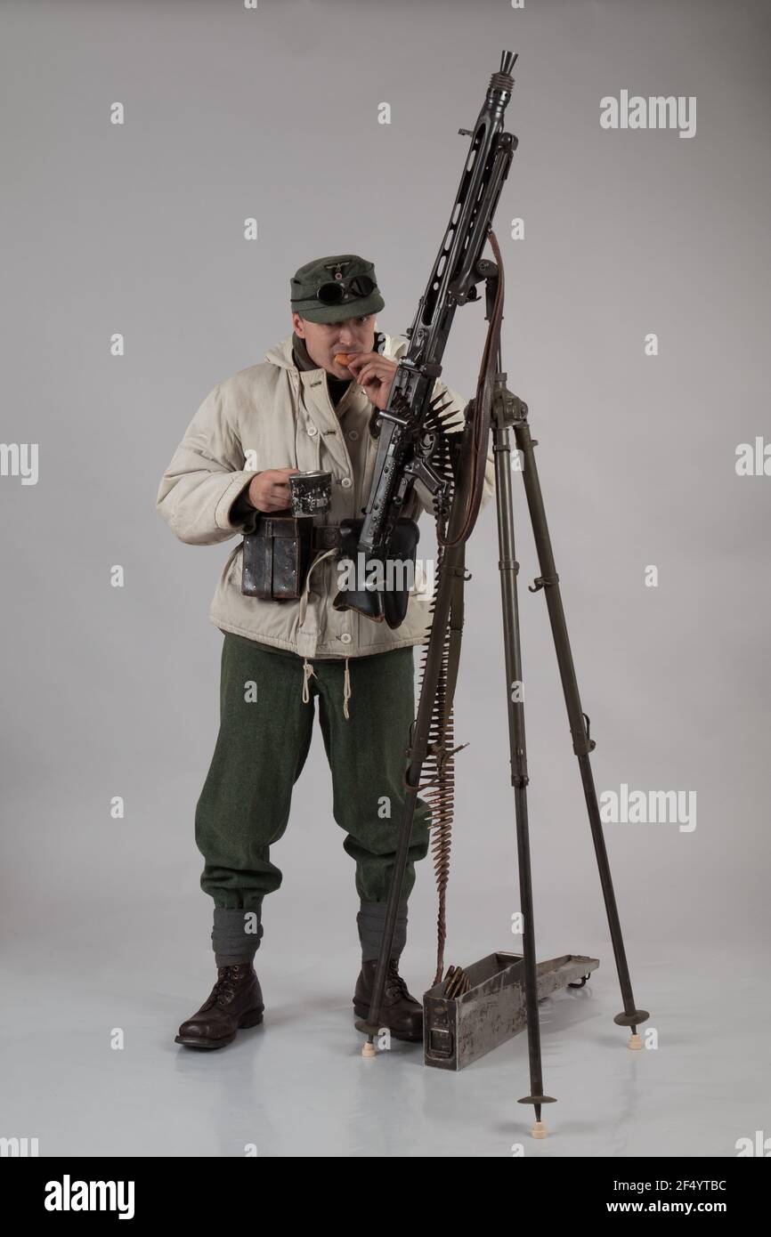 acteur homme dans l'ancien uniforme de montagne d'hiver près de la MG 42 mitrailleuse pendant la deuxième Guerre mondiale pose sur fond gris Banque D'Images