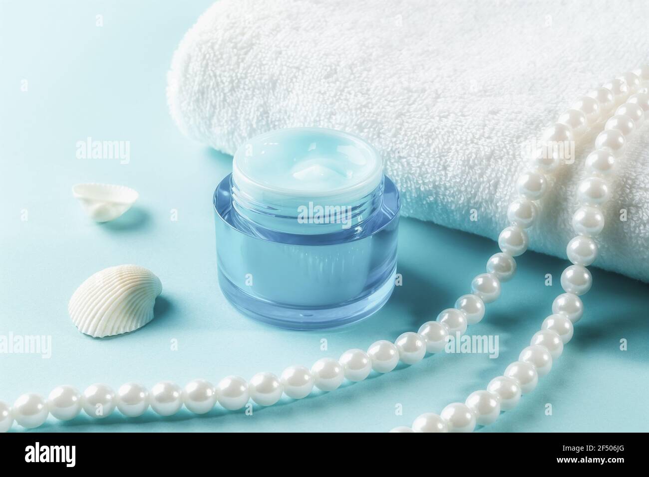 Pot de gel hydratant pour le visage et de perles près d'une serviette  blanche sur une surface en bois bleu. Contenant bleu de crème hydratante  pour le visage. Beauté, soin de la