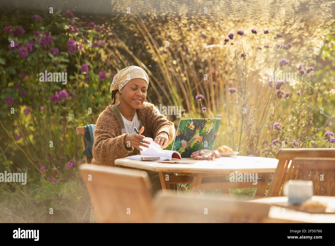 Femme travaillant à un ordinateur portable à une table de café de jardin idyllique Banque D'Images