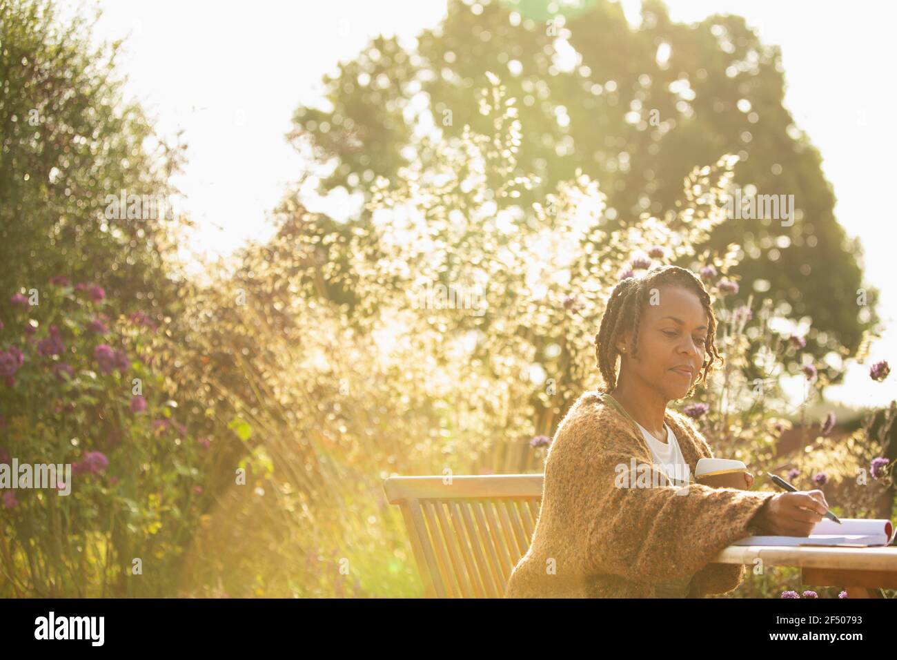 Femme travaillant à une table de café de jardin idyllique ensoleillée Banque D'Images