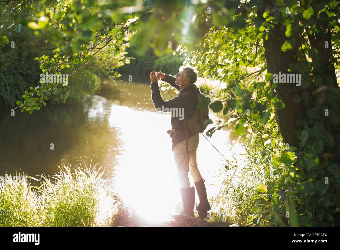 Homme pêche à la mouche dans la rivière idyllique ensoleillée d'été Banque D'Images