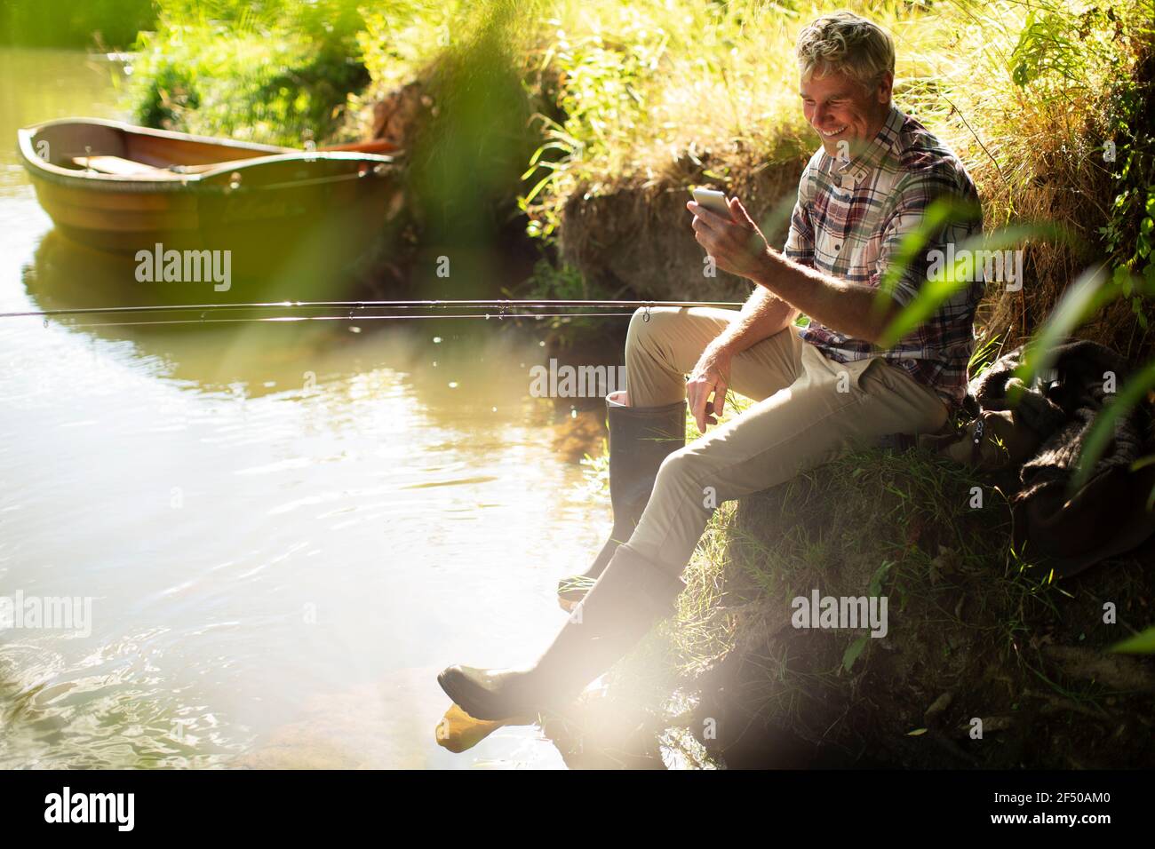 Homme avec smartphone pêche à la mouche à la rivière ensoleillée Banque D'Images