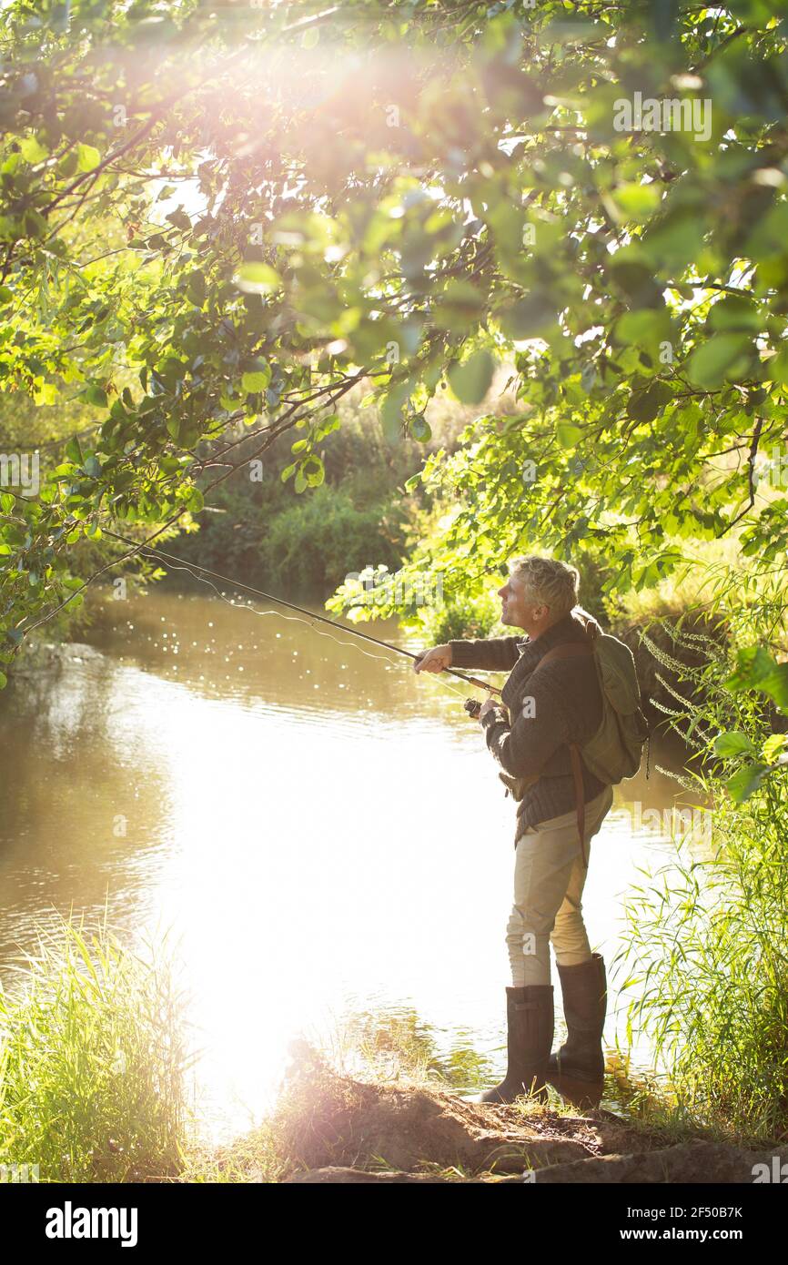 Homme pêche à la mouche sur la rive verte ensoleillée Banque D'Images