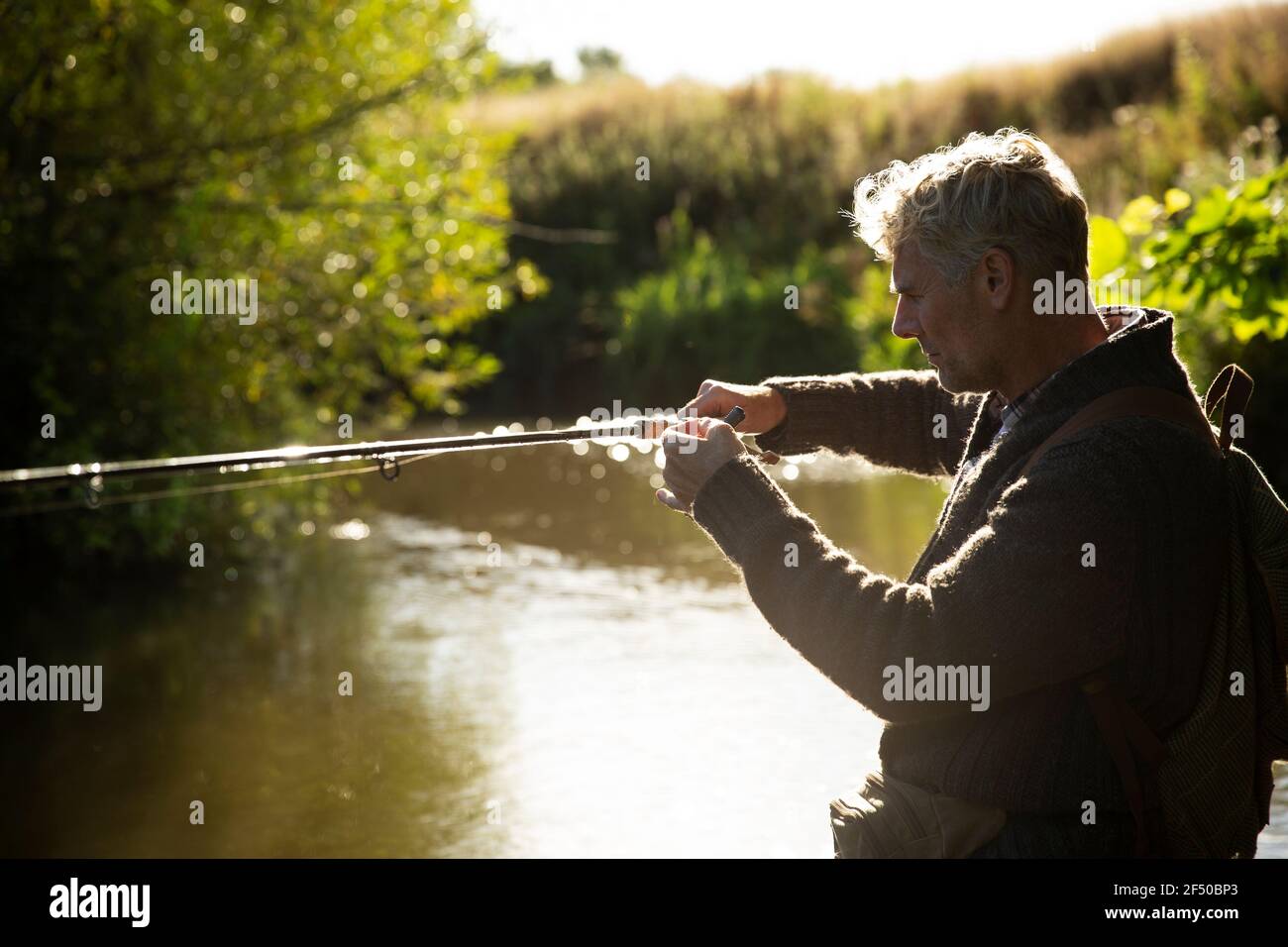 Homme préparant le poteau de pêche à la mouche à la rivière ensoleillée Banque D'Images