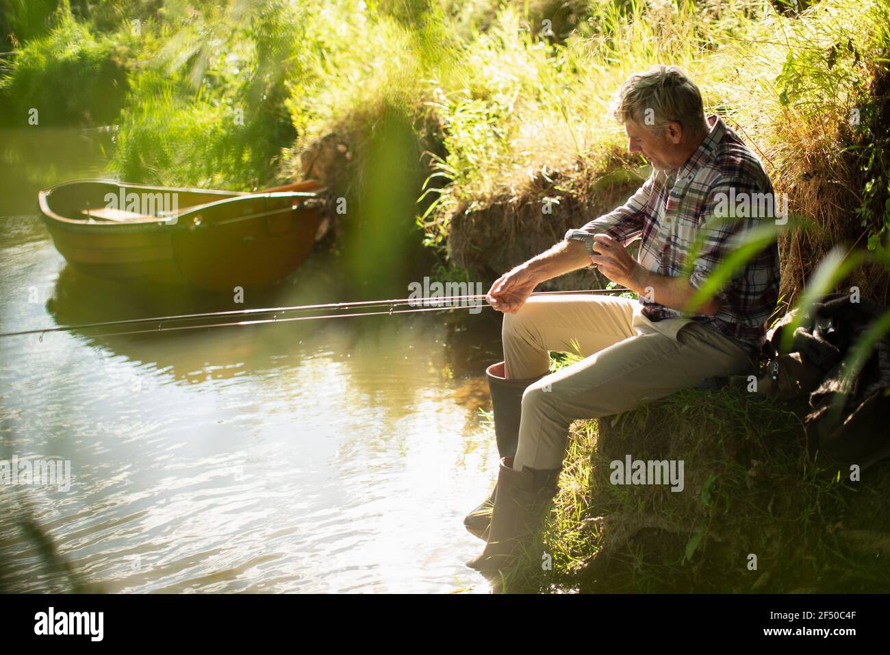 Homme pêche à la mouche sur les manches au bord de la rivière ensoleillée Banque D'Images