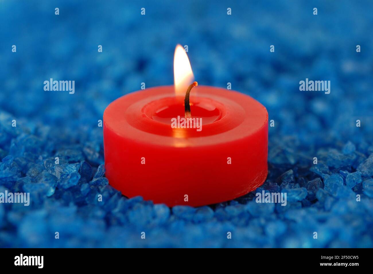 Bougie rouge sur les sels de mer bleus pour le spa. Concentrez-vous sur une mèche. Banque D'Images