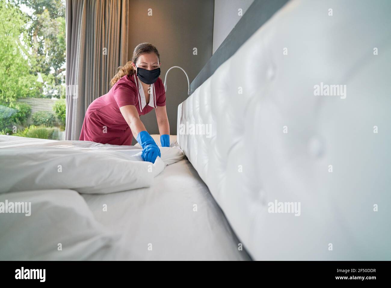 Femme de ménage dans un masque facial faisant le lit à l'hôtel chambre Banque D'Images