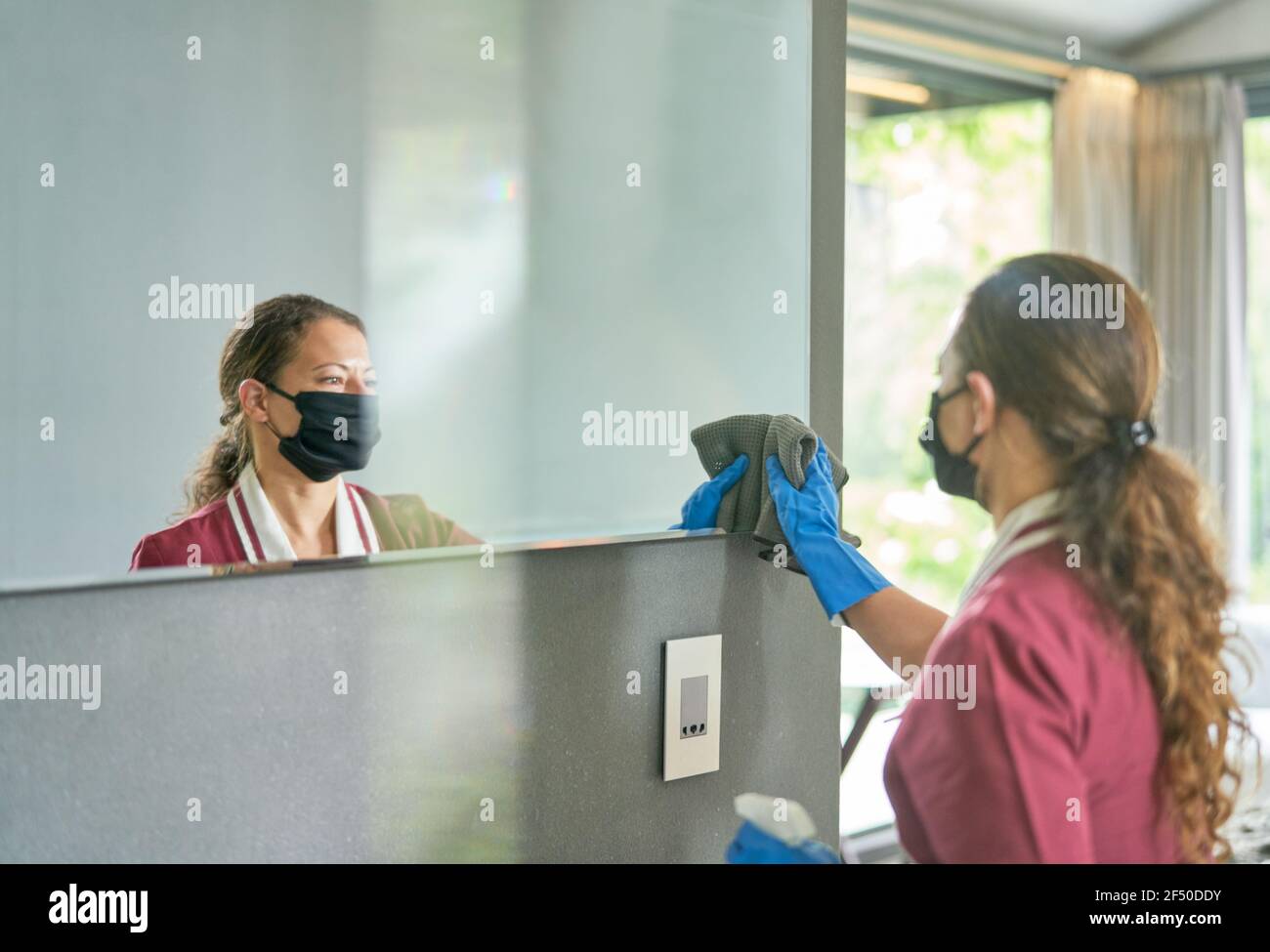 Femme de ménage dans le masque et les gants de nettoyage de la salle de bains miroir Banque D'Images
