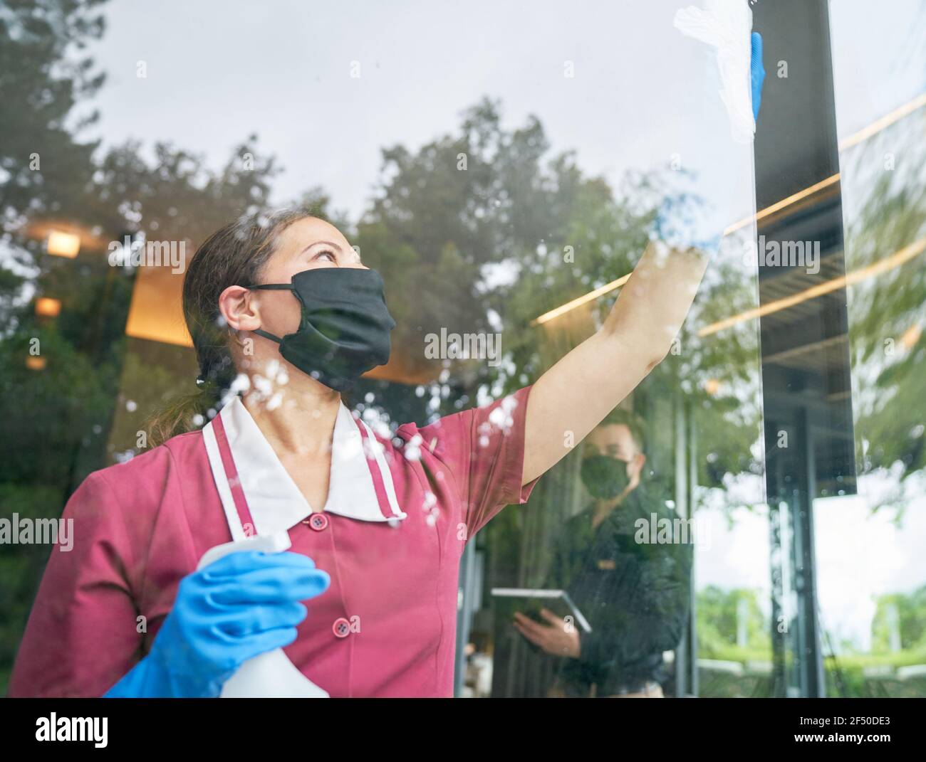 Femme de ménage dans le masque de nettoyage de la fenêtre de l'hôtel Banque D'Images