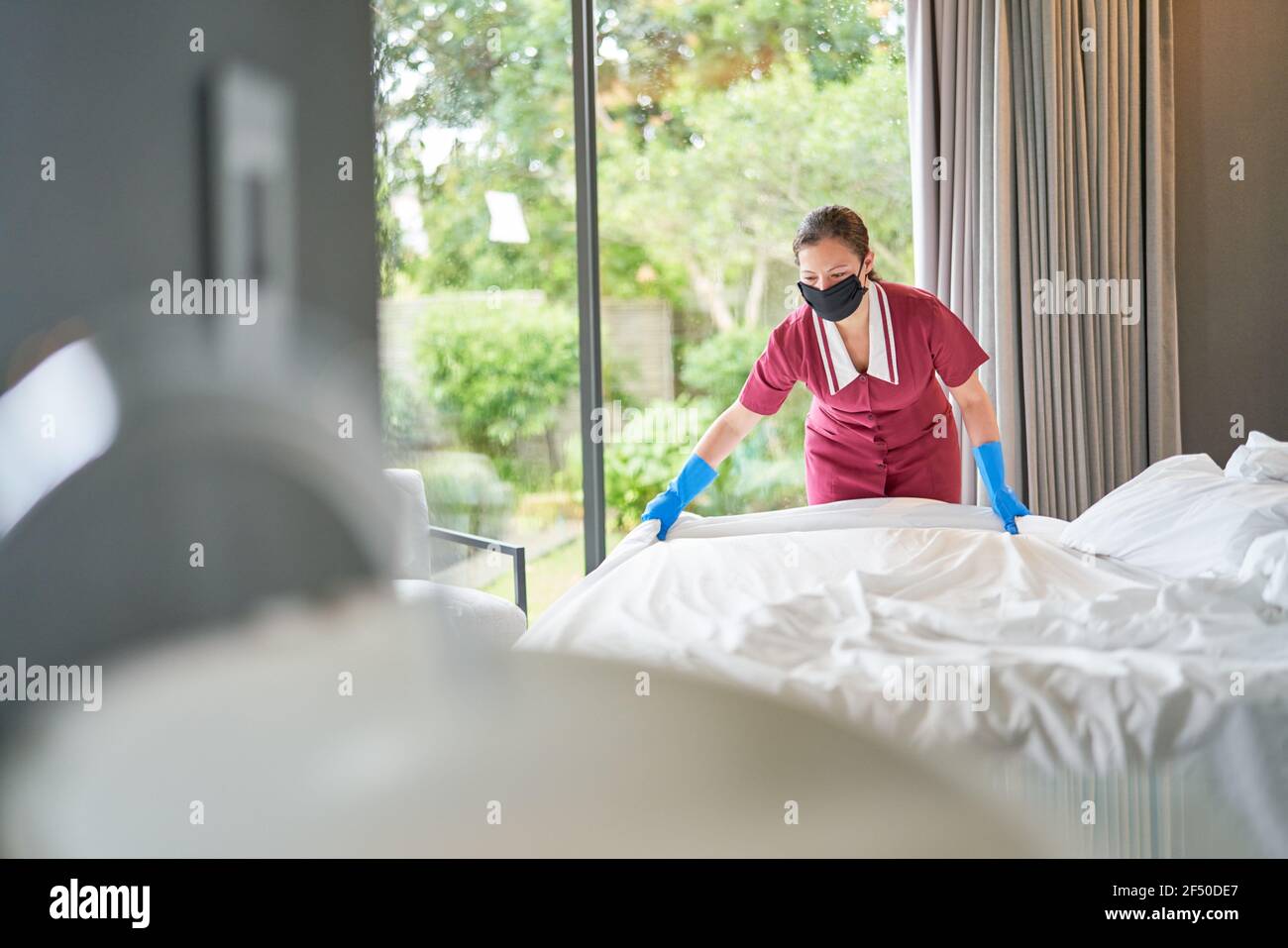 Femme de ménage dans un masque facial faisant le lit à l'hôtel chambre Banque D'Images