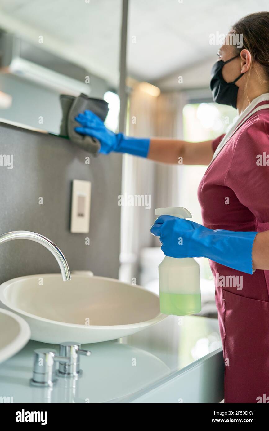Femme de ménage dans le masque et les gants de nettoyage de la salle de bains Banque D'Images