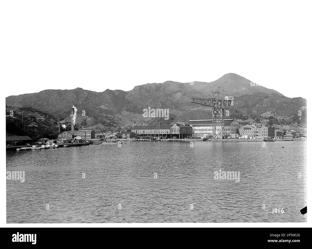 Nagasaki (Japon). Installations portuaires avec des bâtiments de stockage et une tour de grue, dans la chaîne de montagne d'arrière-plan Banque D'Images