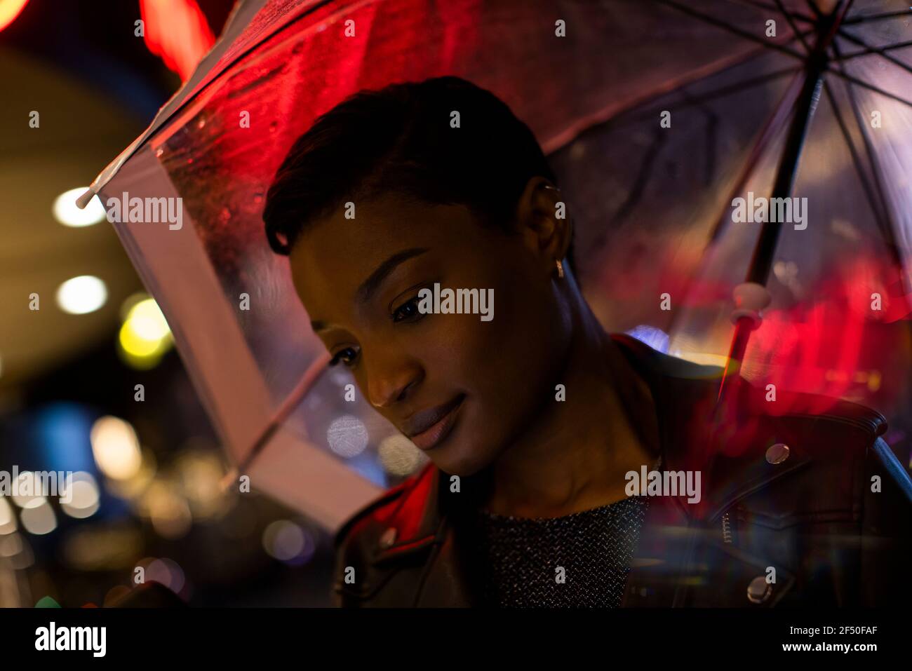 Jeune femme sous parapluie et lumières de néon la nuit Banque D'Images