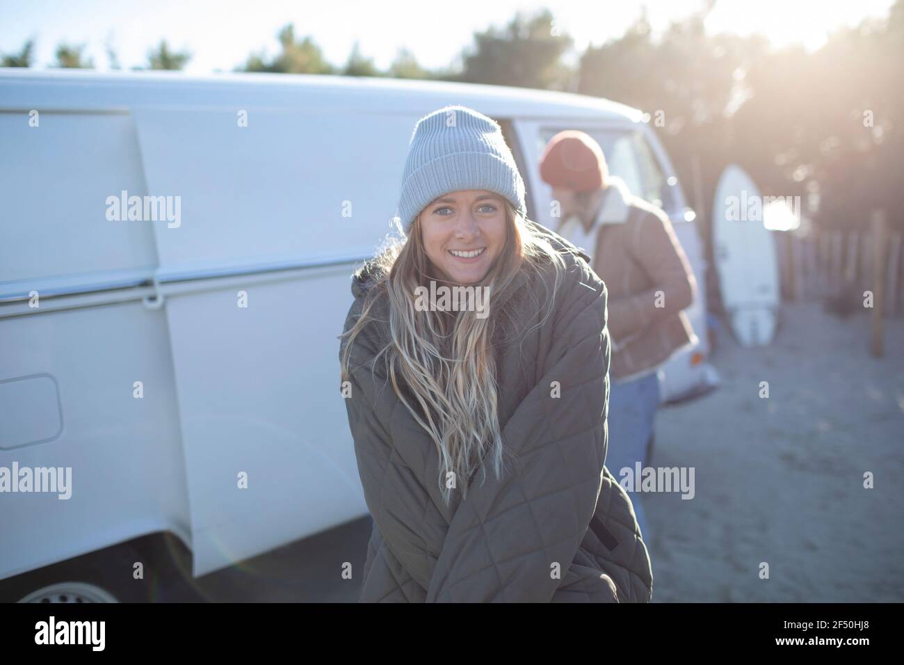 Portrait bonne jeune femme surfeuse en manteau et chapeau à l'extérieur fourgonnette ensoleillée Banque D'Images