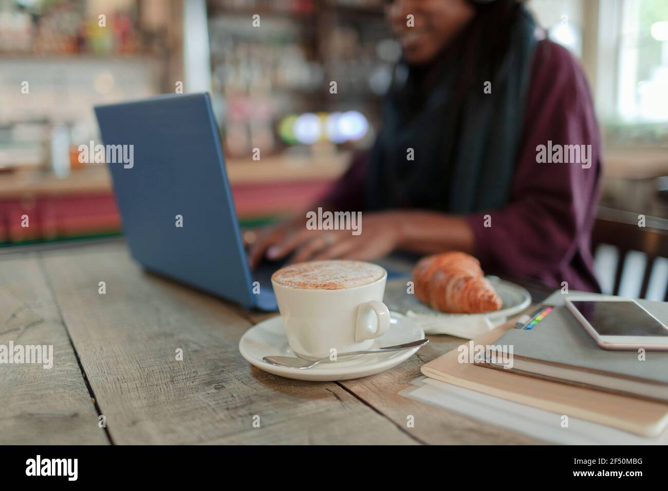 Femme travaillant sur un ordinateur portable à côté d'un cappuccino et d'un croissant café Banque D'Images