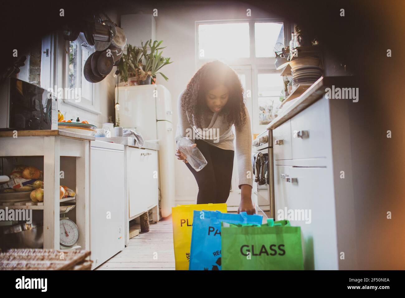 Femme triant le recyclage dans des sacs sur le plancher de la cuisine Banque D'Images