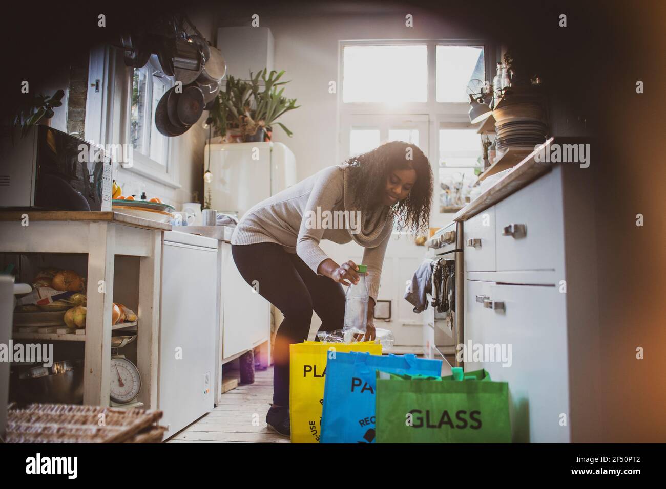 Jeune femme triant le recyclage sur le sol de la cuisine Banque D'Images