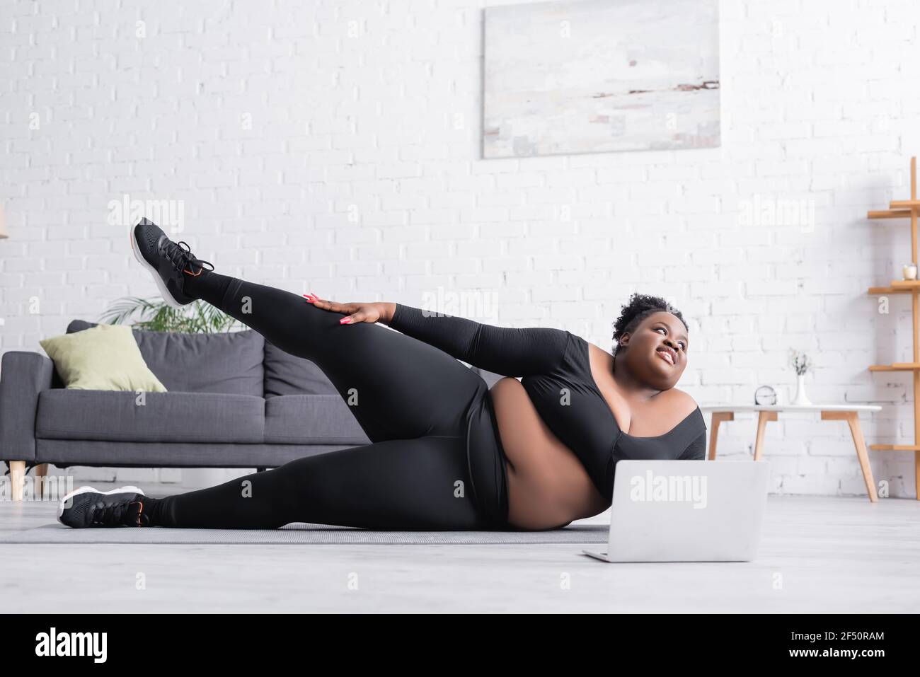 une femme africaine américaine de taille plus joyeuse s'exerçant près d'un ordinateur portable ...