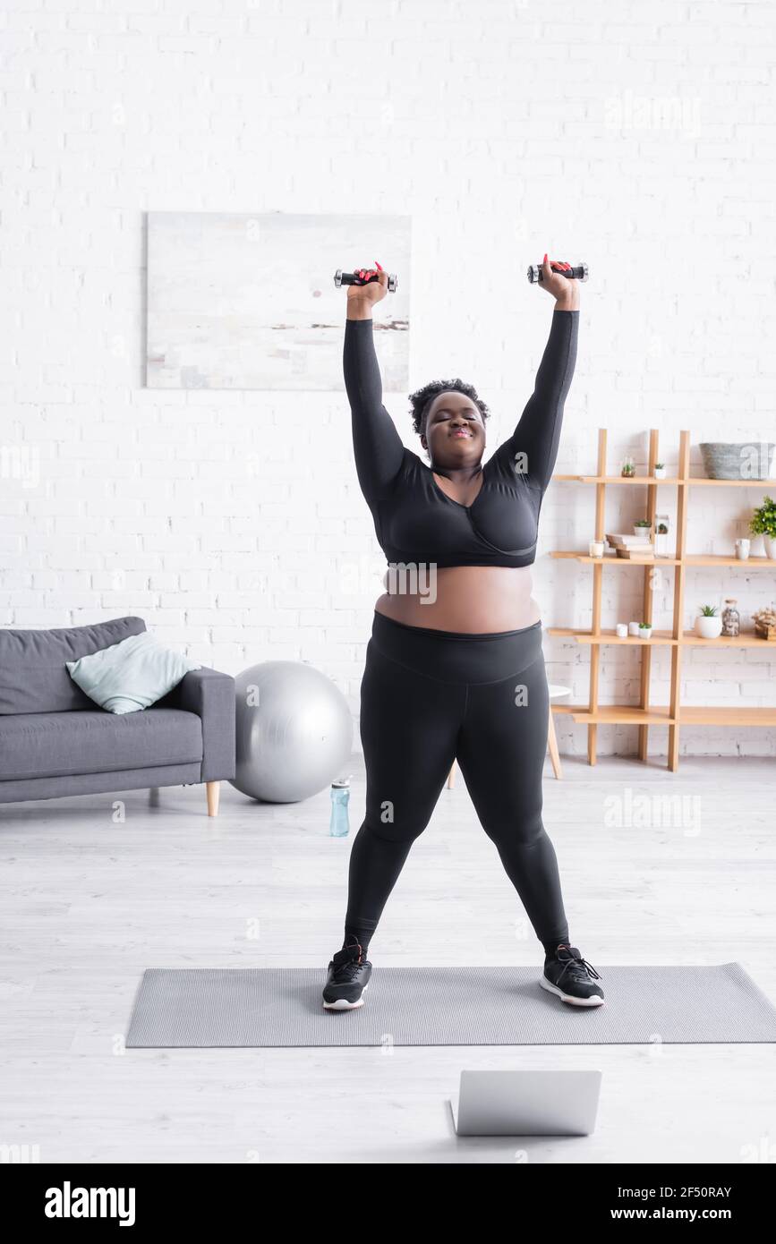 femme afro-américaine de grande taille dans les vêtements de sport faites  de l'exercice avec des haltères dans la salle de séjour Photo Stock - Alamy