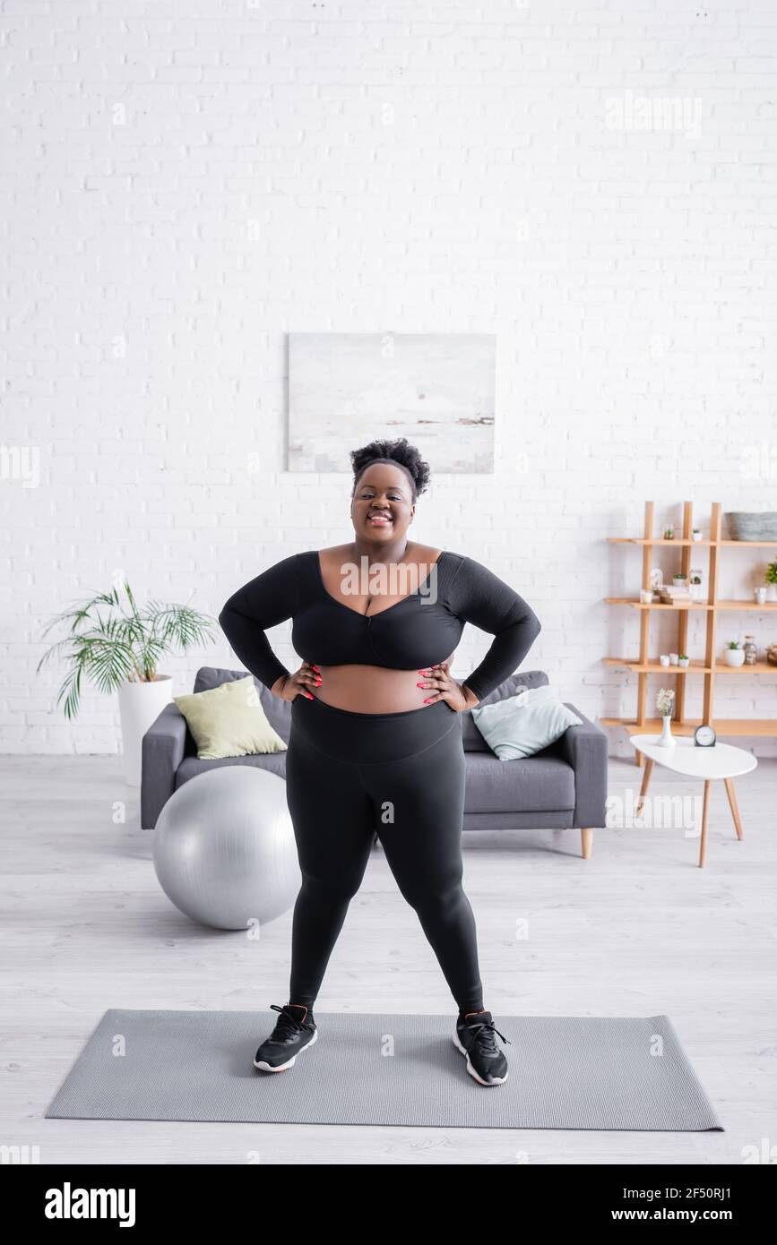 femme afro-américaine de grande taille dans les vêtements de sport debout,  les mains sur les hanches, sur le tapis de fitness Photo Stock - Alamy