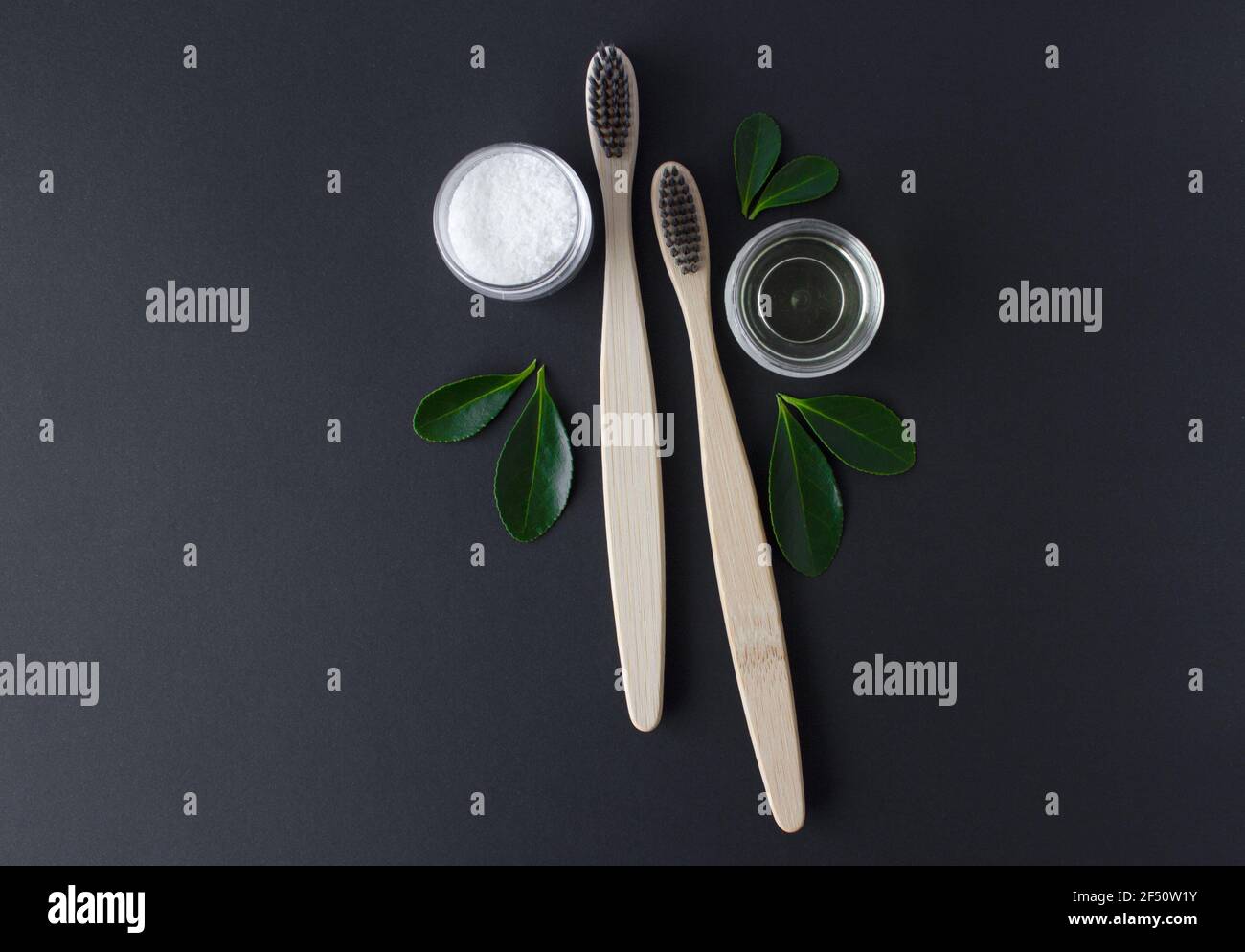 deux brosses à dents écologiques en bambou en bois, dentifrice à l'huile de coco et feuilles vertes sur fond noir. Banque D'Images