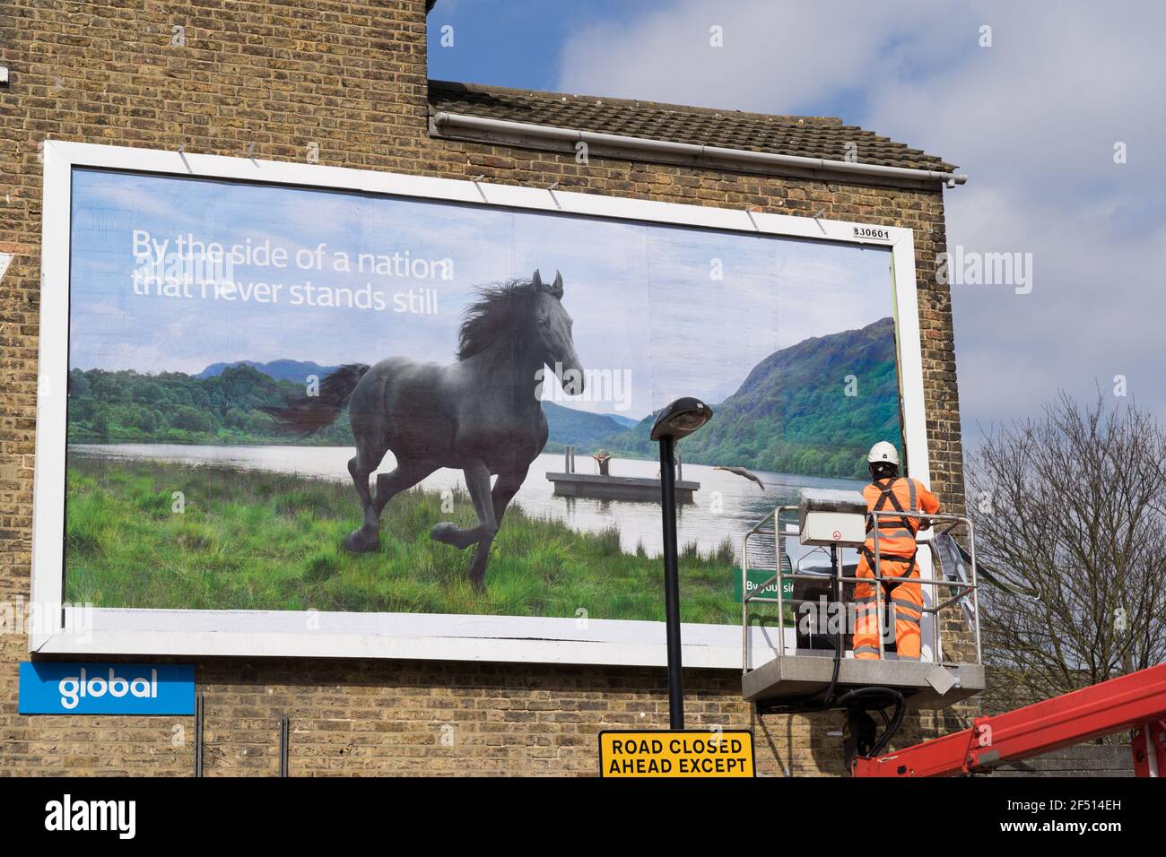 Man termine le dernier panneau de publicité commerciale sur Billboard, plate-forme de sécurité soutenue par une grue, Londres Banque D'Images