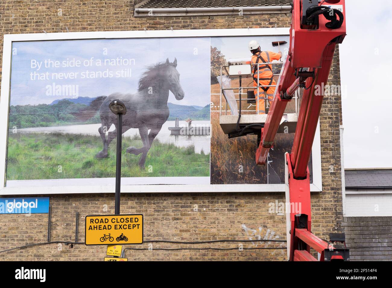 Un homme un homme colle une nouvelle publicité commerciale sur Billboard, plate-forme de sécurité soutenue par une grue, Londres Banque D'Images