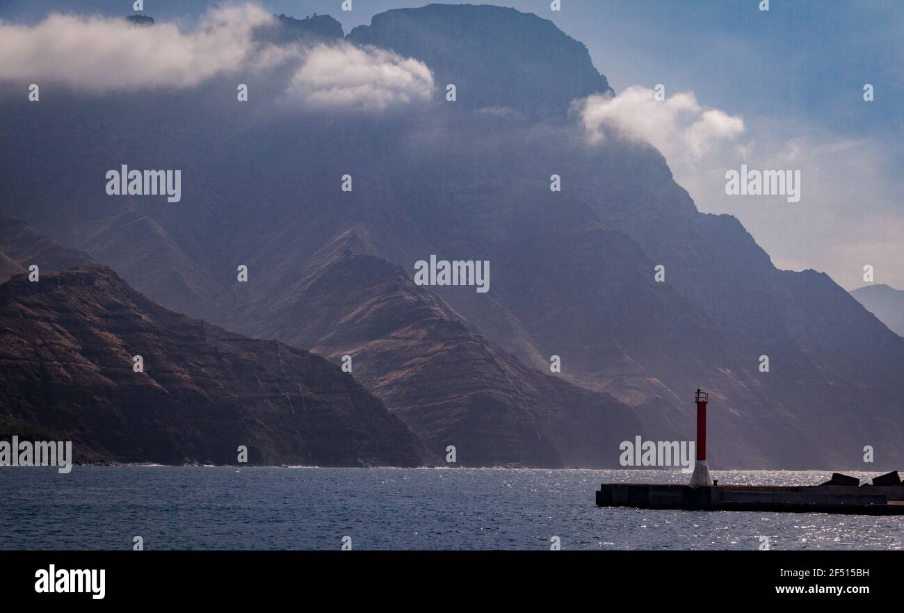 Détail d'une petite balise rouge et blanche à côté du mer avec de grandes montagnes couvertes de nuages en arrière-plan Banque D'Images