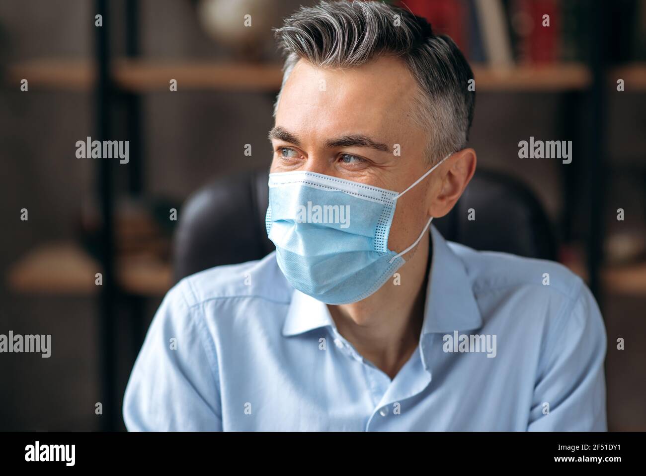 Un gros plan d'un homme âgé, d'un responsable ou d'un employé de bureau caucasien à cheveux gris qui a réussi, le chef d'entreprise portant un masque médical, dans une chemise élégante, regarde loin. Prévention, précautions et protection Banque D'Images