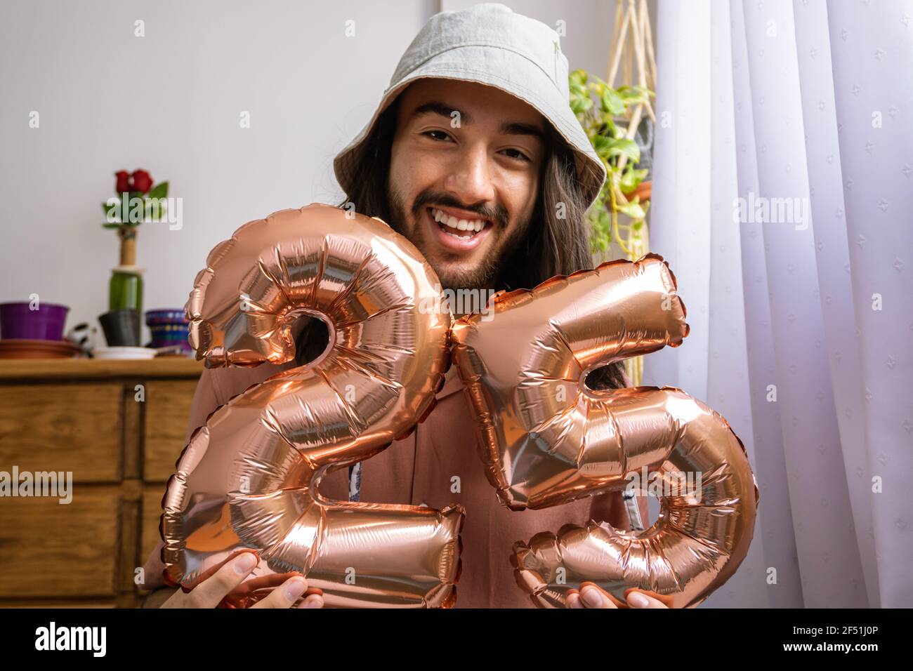 Beau jeune homme latino-asiatique tenant une montgolfière métallique, célébrant son 25e anniversaire. Ballon métallique avec le numéro 25. Banque D'Images