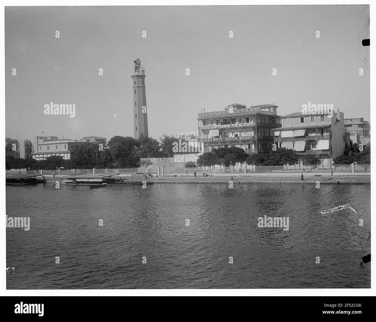 Port Said, Égypte. Vue depuis un bateau à vapeur en haute mer de Hapag sur les bandes côtières du canal de Suez avec quai à bateaux, phare et publicité pour les produits anglais Banque D'Images