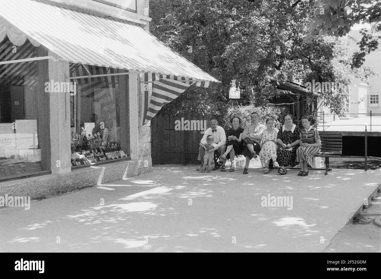 Enregistrements privés. Formation de groupe sur un banc à côté d'un magasin avec publicité pour Asbach Old Banque D'Images