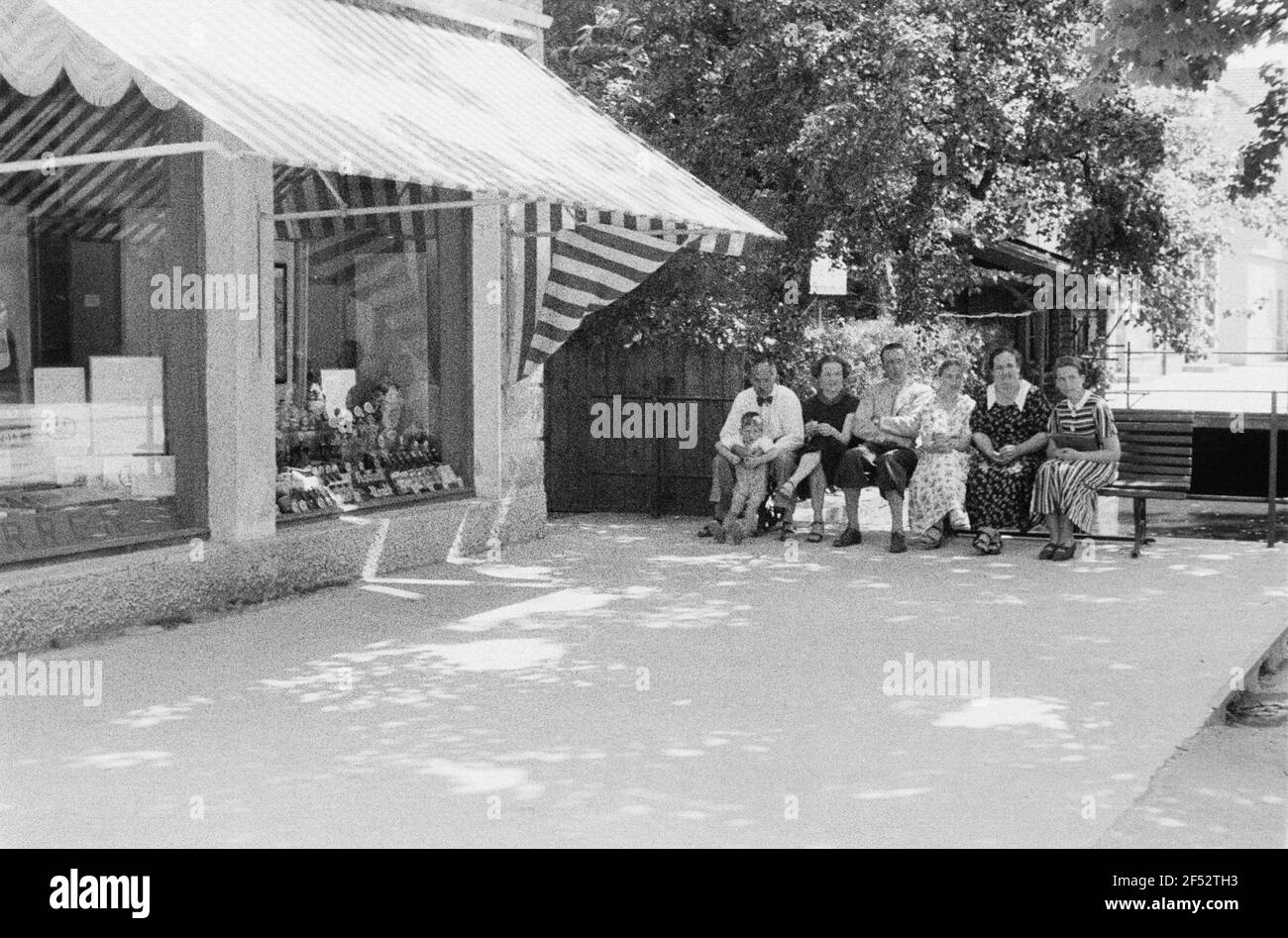 Enregistrements privés. Formation de groupe sur un banc à côté d'un magasin avec publicité pour Asbach Old Banque D'Images