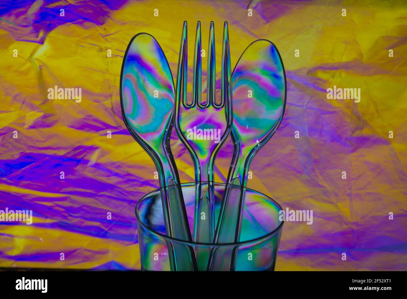 Un effet surréaliste créé avec une lentille polarisée de couverts en plastique sur un fond de papier froissé aux couleurs vives dans les tons violet et jaune. Banque D'Images