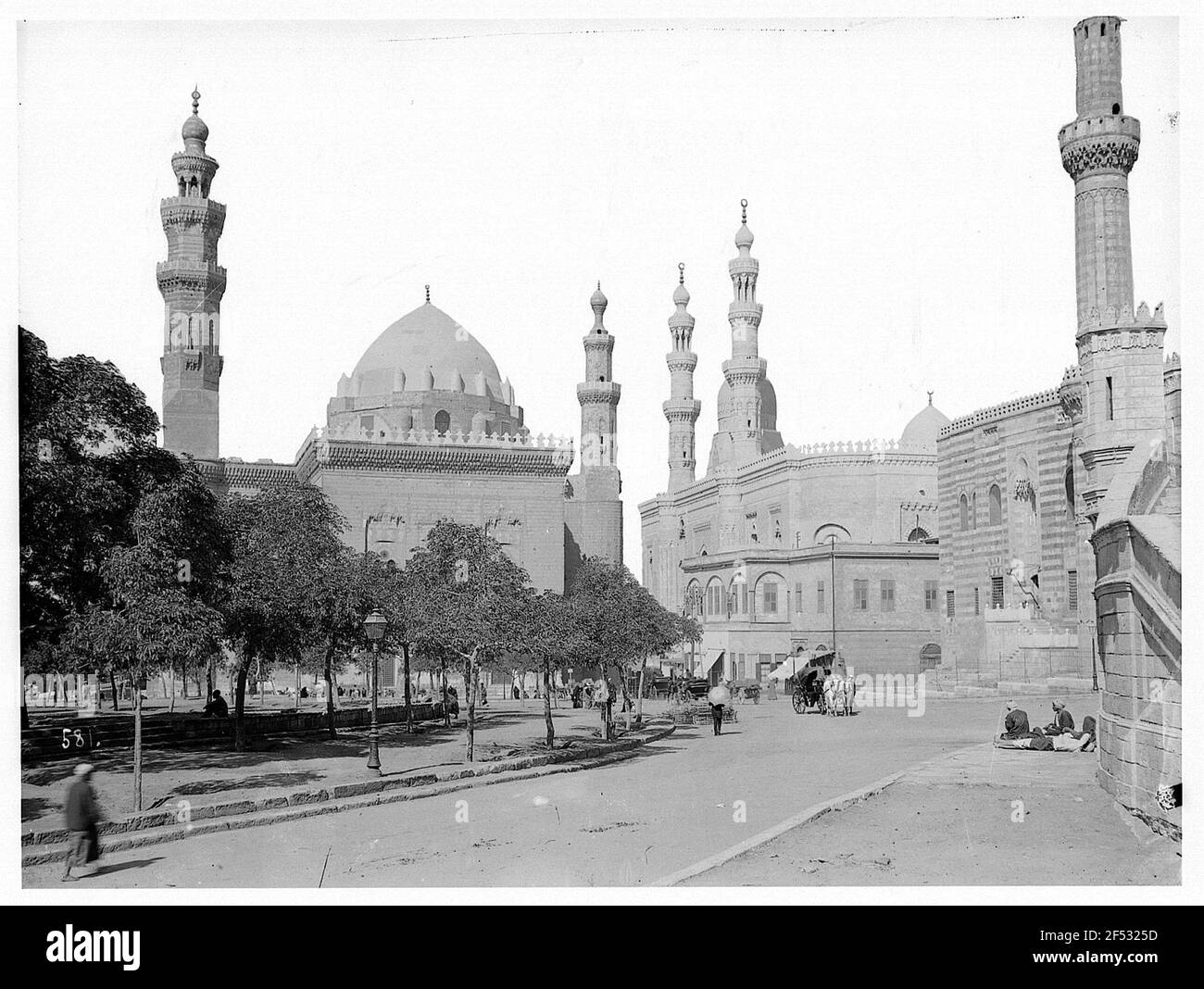 Le Caire (Égypte). Locaux avec chariots à ânes et chariots tirés par des chevaux dans une rue. Vue sur la mosquée du Sultan Hassan Banque D'Images