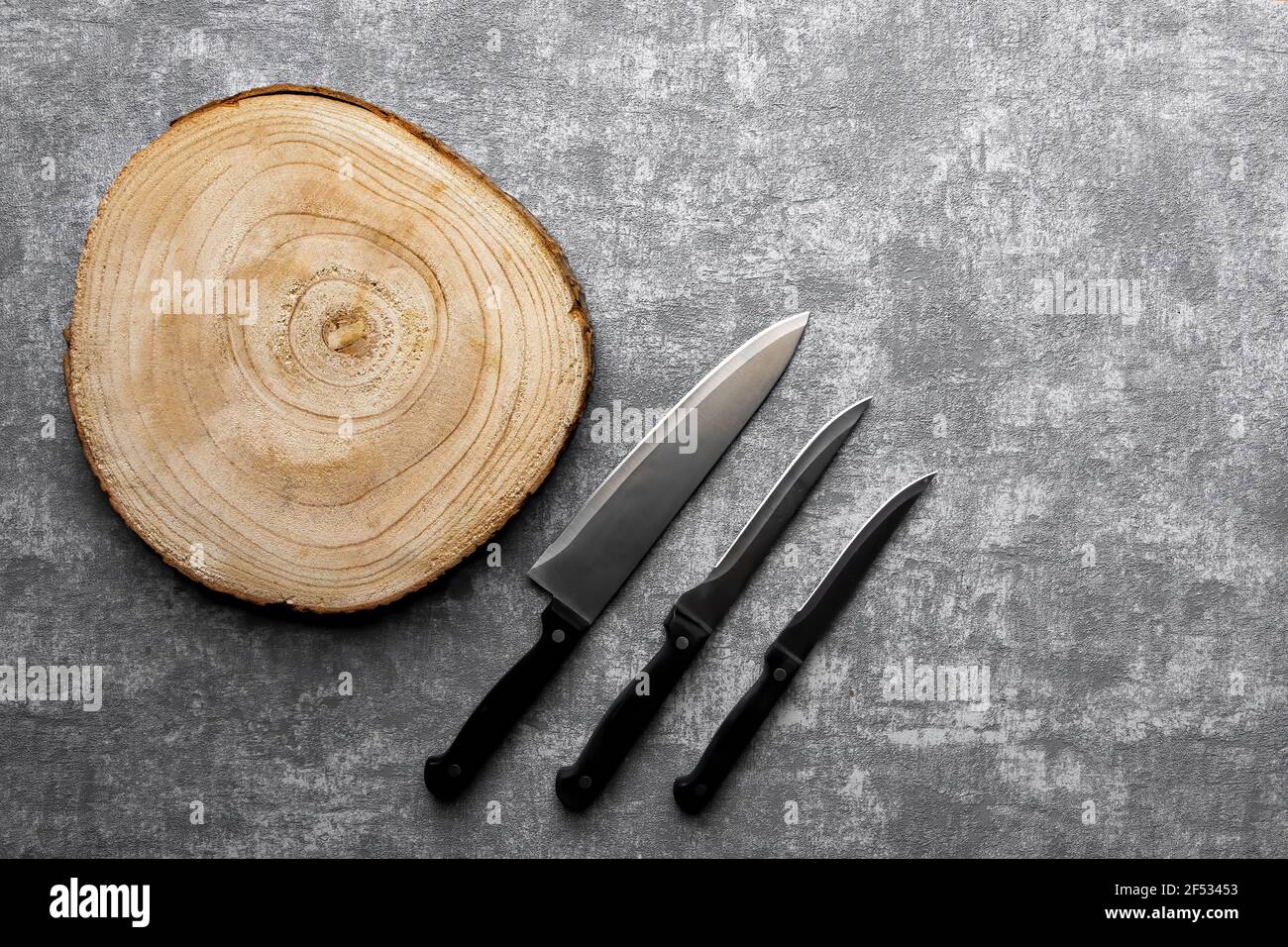 Bord de coupe en bois et 3 couteaux différents sur fond en béton gris. Banque D'Images