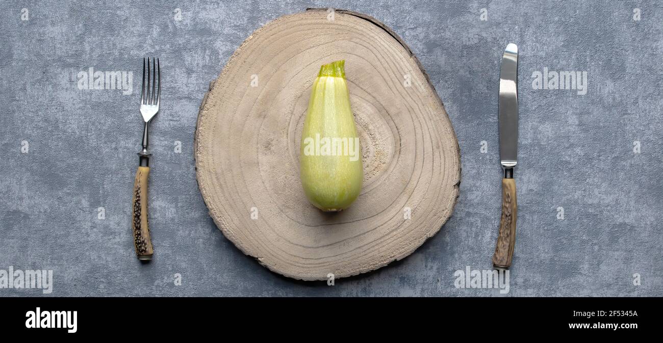 Courgette verte simple mûre fraîche sur la planche à découper avec fourchette et couteau sur fond gris table de cuisine. Banque D'Images