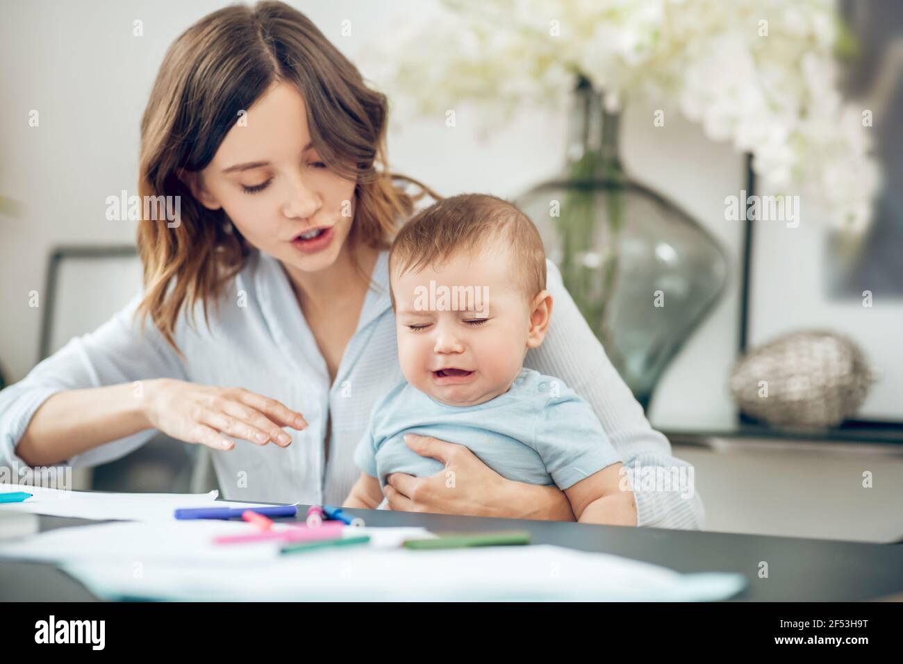 Jeune mère apaisante pleurs bébé assis à la table Banque D'Images