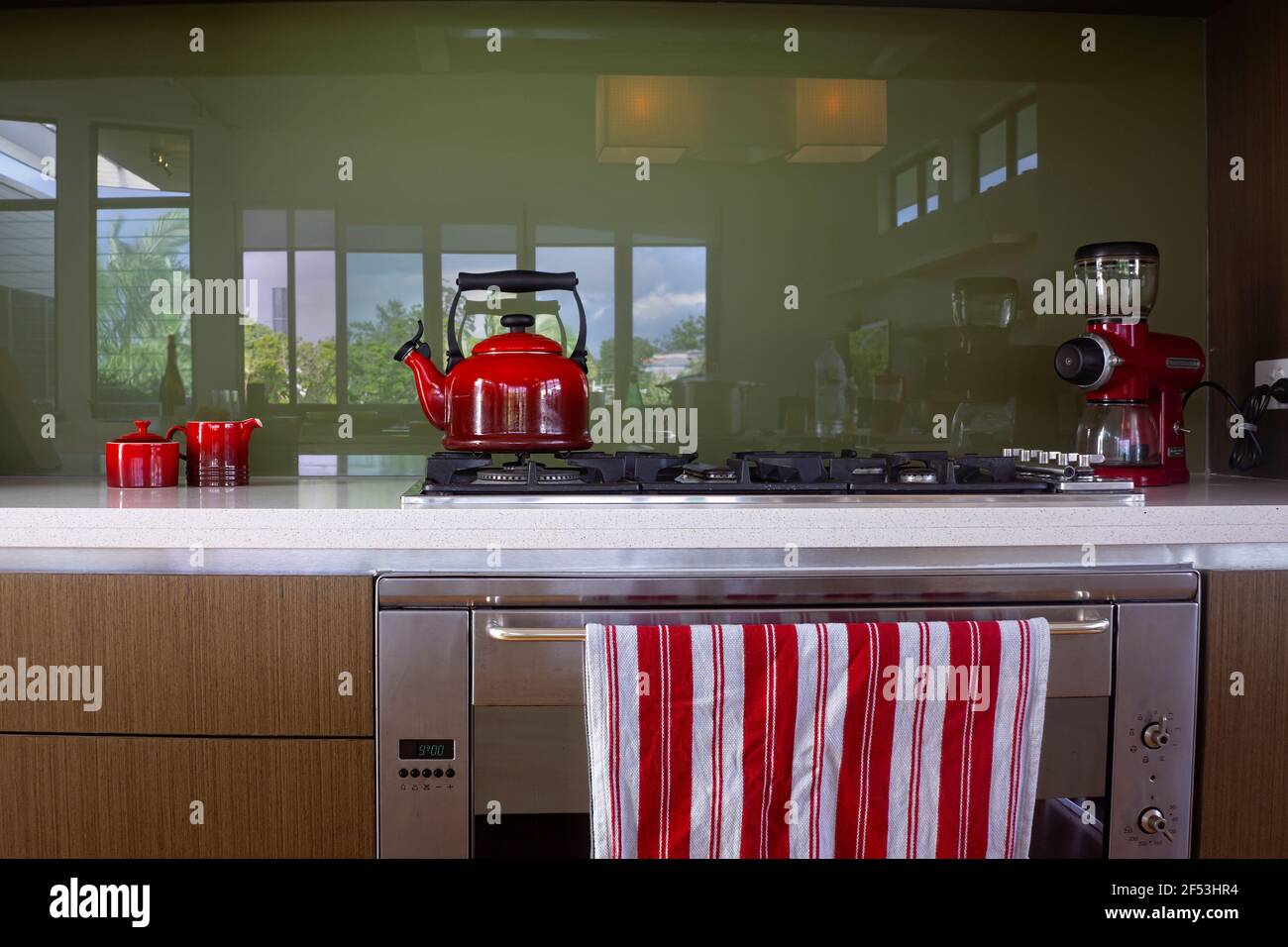 Appareils rouges comprenant une bouilloire, un moulin à café, un bol à sucre et un crémier sur un banc de cuisine avec un dessus de cuisson au gaz et une théière à rayures rouges et blanches Banque D'Images