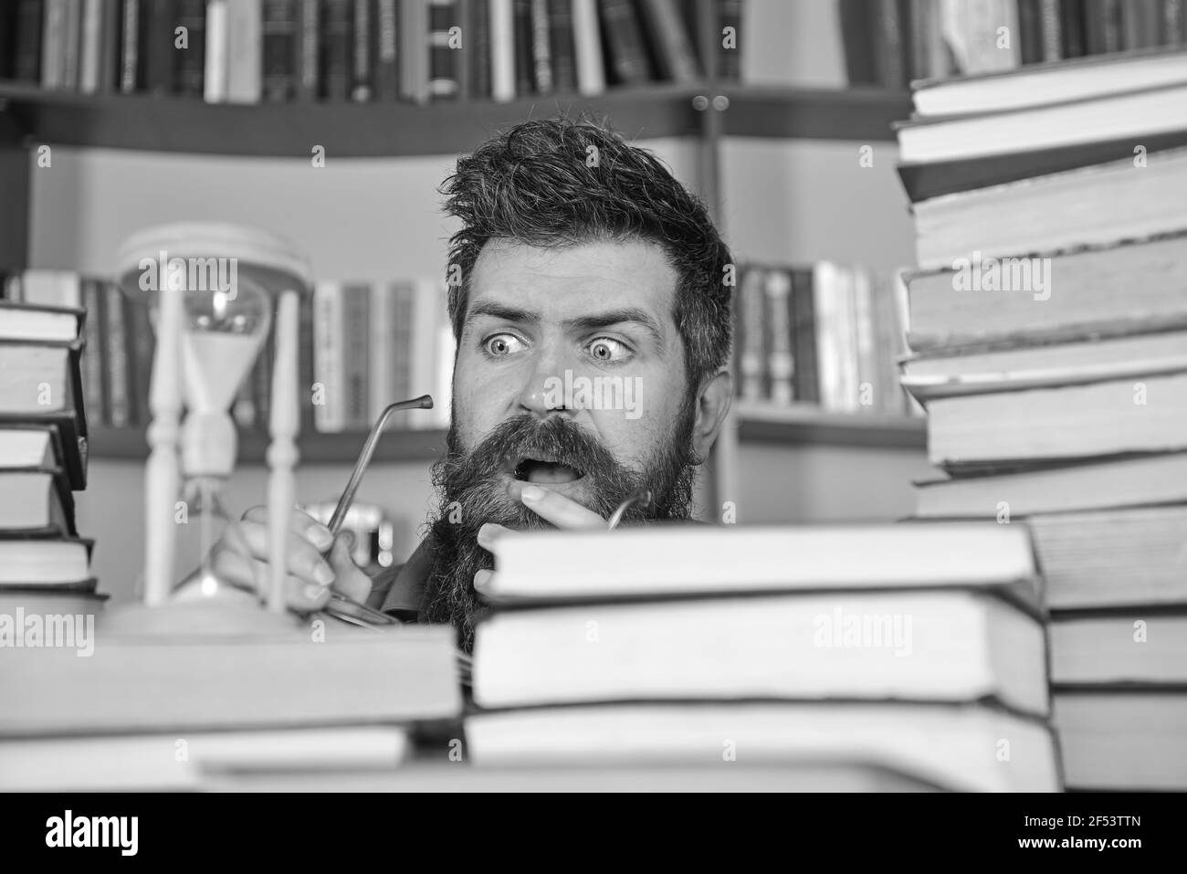 Homme, scientifique regarde le sablier. Professeur ou étudiant avec la barbe étudiant dans la bibliothèque. L'homme sur le visage sérieux et choqué regarde le temps est passé Banque D'Images