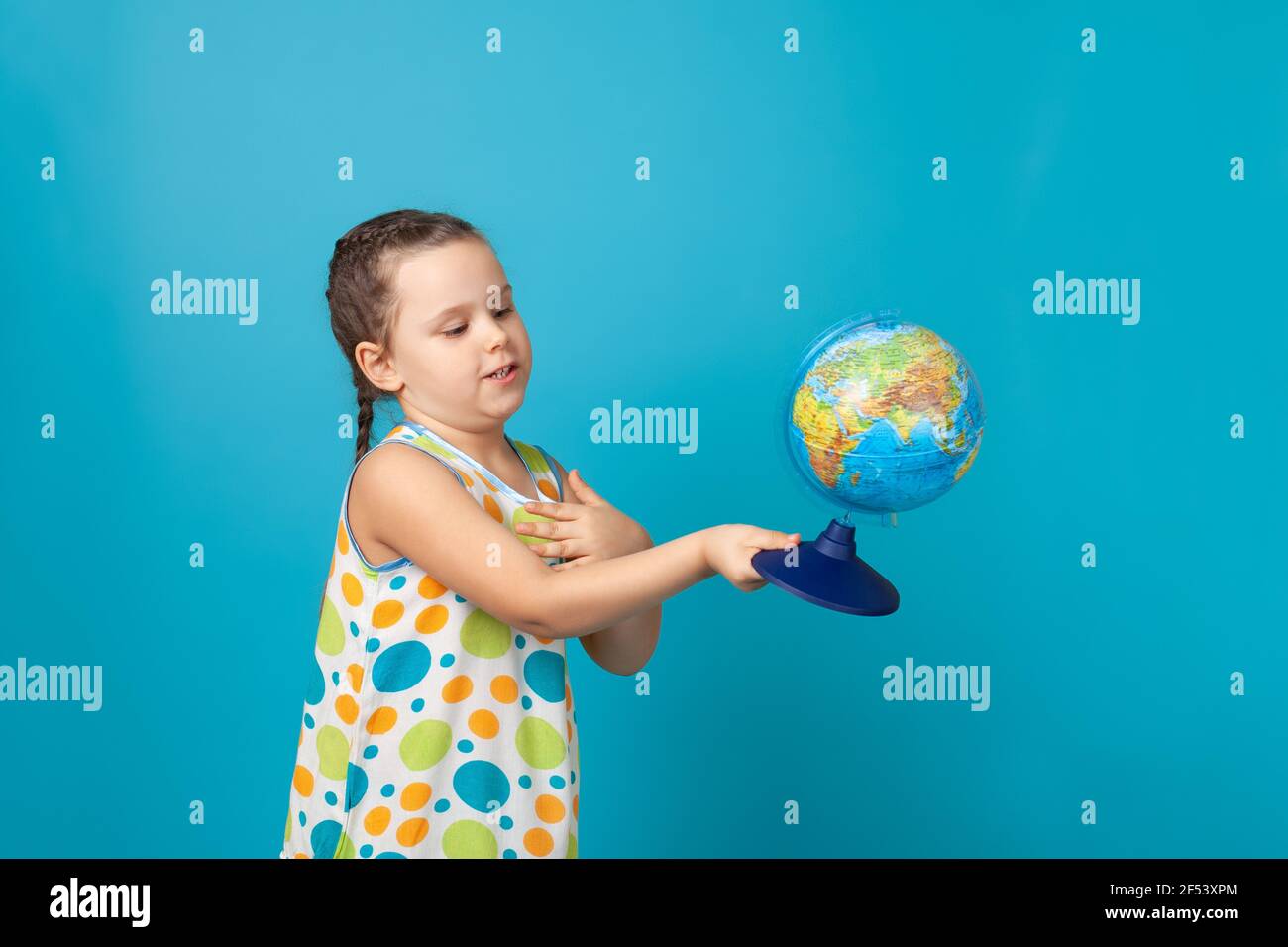 portrait d'une fille positive dans une robe blanche d'été tournant un globe et étudiant la géographie, isolée sur un fond bleu Banque D'Images