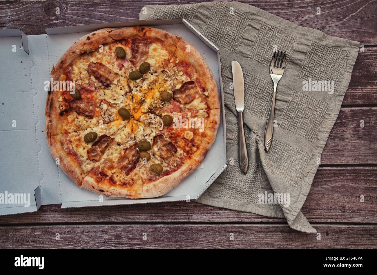 Pizza à emporter délicieuse sur une table en bois. Photo rognée des mains prenant un morceau de pizza Banque D'Images
