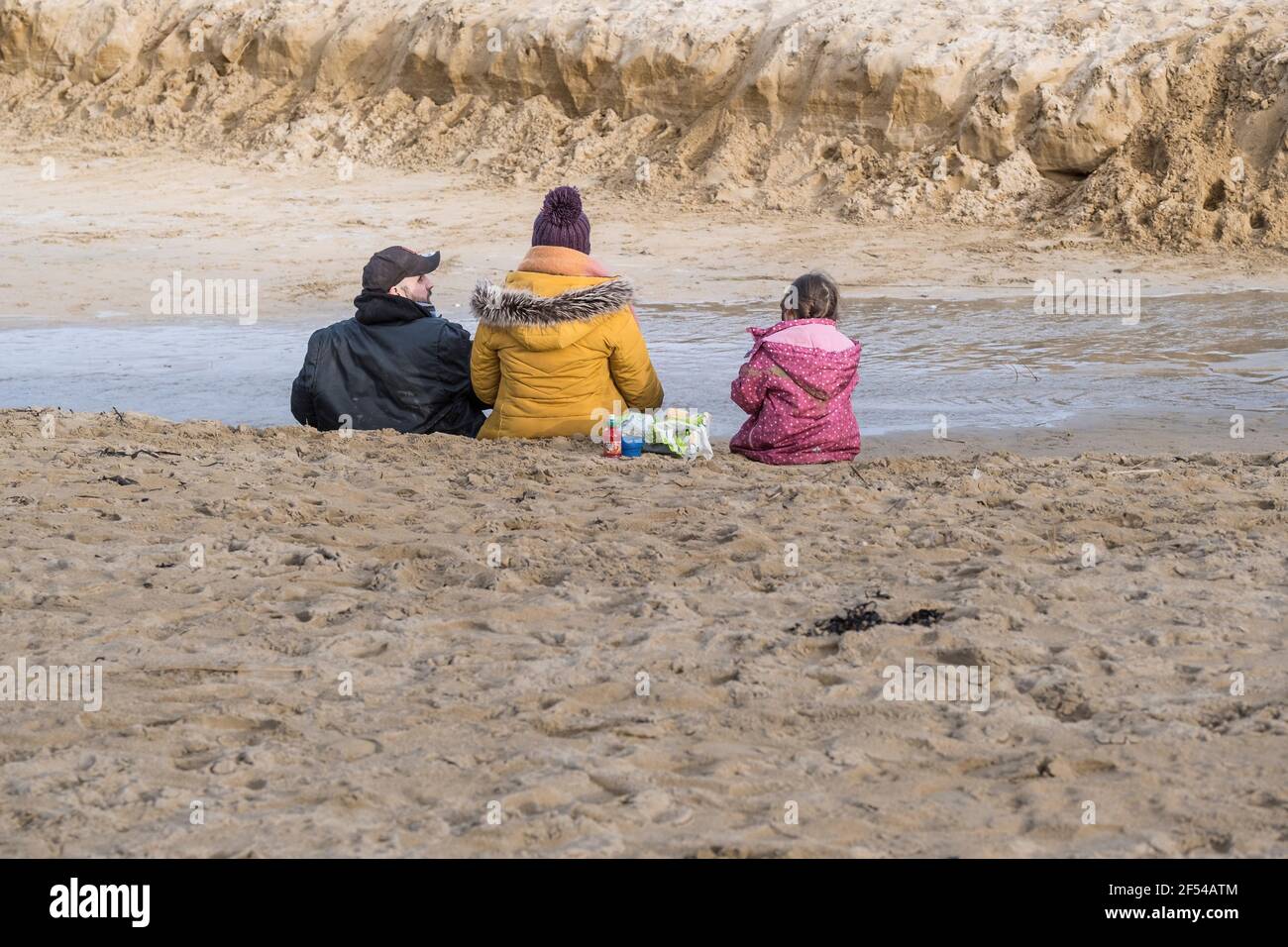 Une famille assise sur Crantock Beach par temps froid à Newquay, en Cornouailles. Banque D'Images