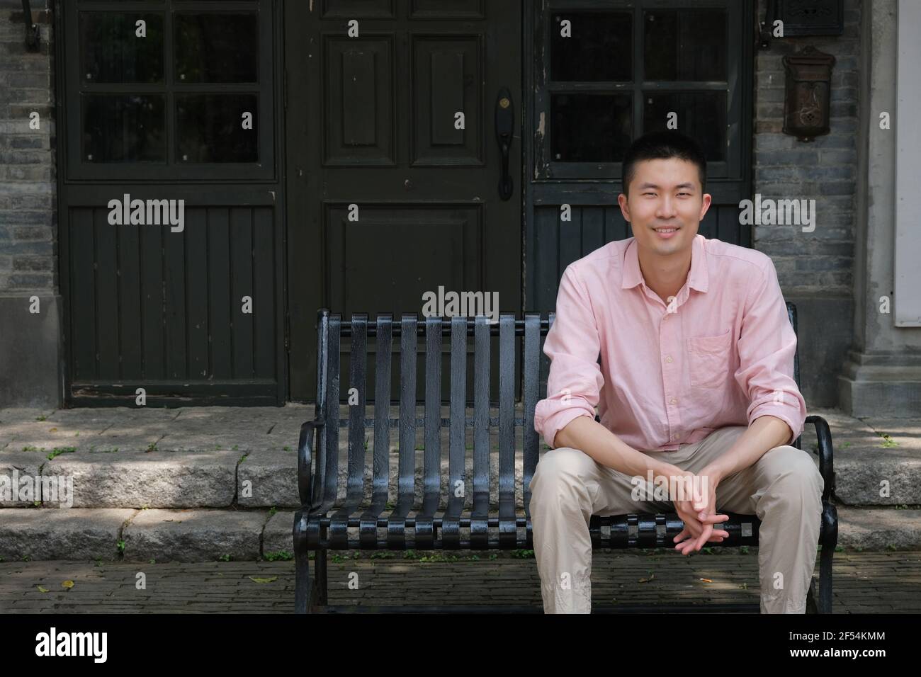 Jeune homme asiatique souriant assis sur le banc devant le café Banque D'Images