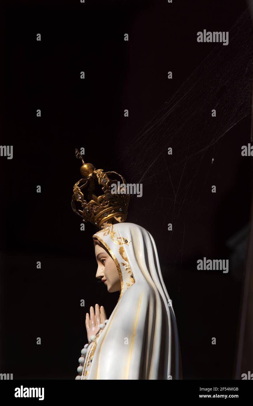Priant la statue de Madonna Fatima avec une toile d'araignée sur sa couronne dans une église vide sombre. Contexte religieux. Miséricorde, miracle, espoir, concepts de prière. Banque D'Images